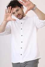 Home Young man in glasses poses playfully in white shirt, light background.